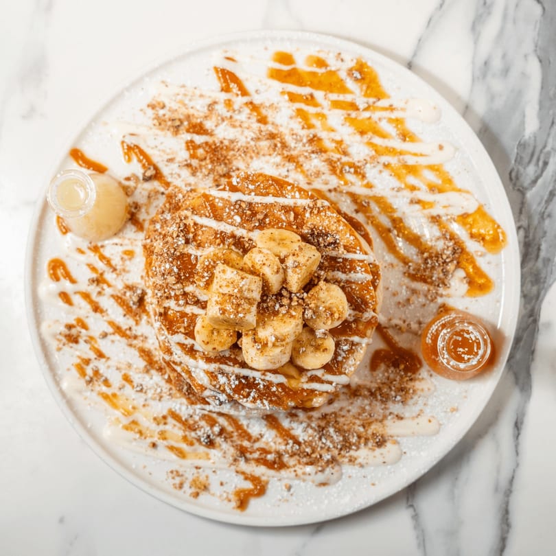 Golden waffles topped with sliced bananas, powdered sugar, nuts, caramel, and cream drizzle.