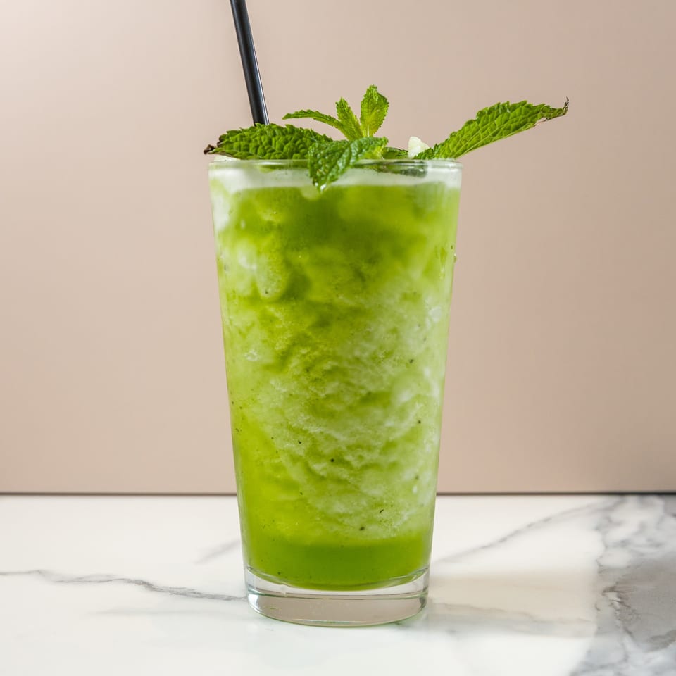 Refreshing green smoothie with mint leaves and a black straw, on a marble surface.