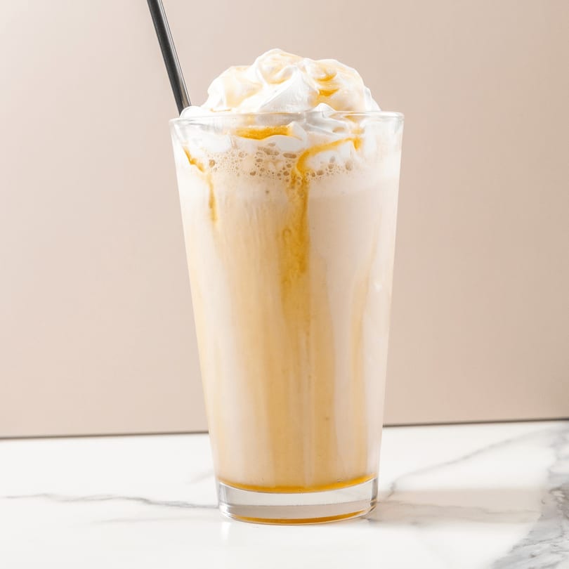 Caramel frappe with whipped cream and a black straw on a marble surface.