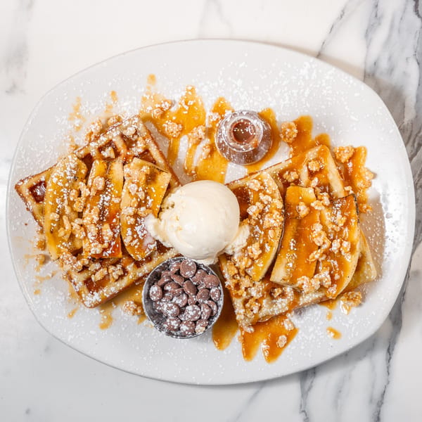 Waffles with caramelized bananas, ice cream, chocolate chips, caramel sauce, and powdered sugar.