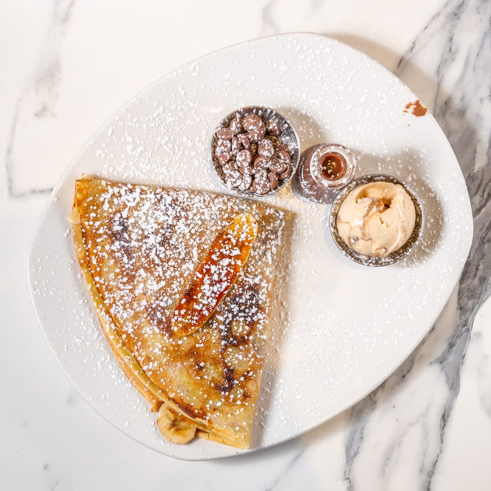 Banana crepe dusted with powdered sugar, served with chocolate chips, caramel, and ice cream.