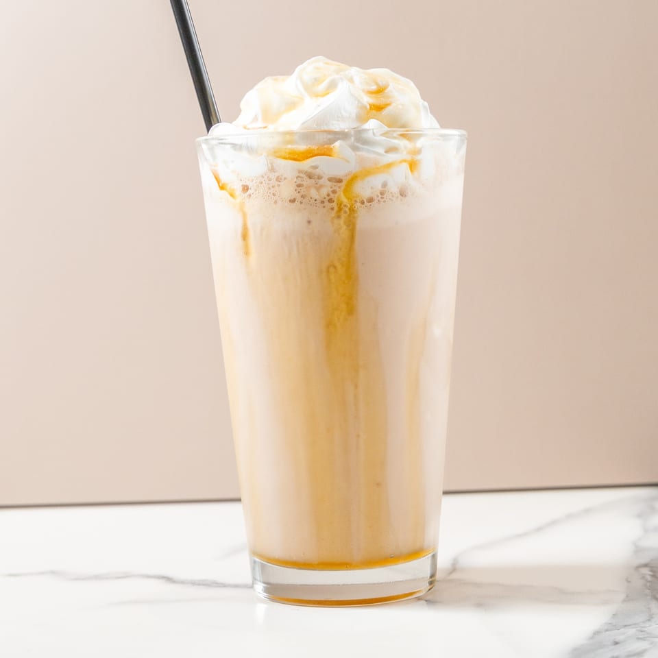 Caramel frappe with whipped cream and a black straw on a marble counter.